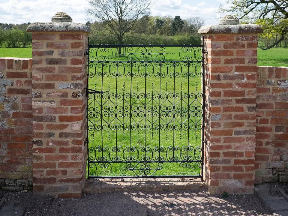 Example of a decorative wrought iron pedestrian gate between brick pillars